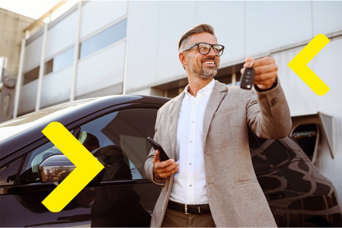 Gospodin drži ključeve automobila u jednoj ruci i pametni telefon u drugoj, stojeći pored crnog automobila