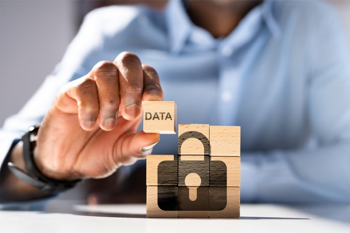 Osoba postavlja drvenu kocku s oznakom "Podaci" na druge kocke koje prikazuju simbol brava, što predstavlja sigurnost i zaštitu podataka.