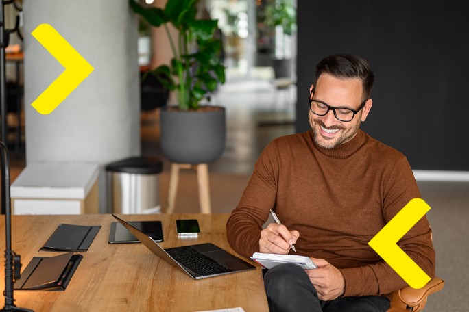 Osoba bilježi bilješke dok sjedi za stolom s prijenosnim računalom u radnom okruženju